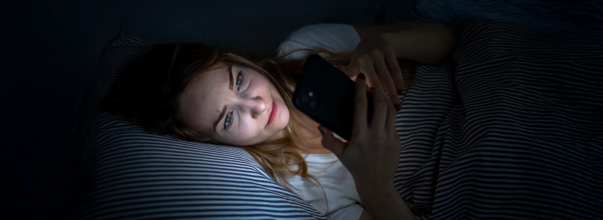 A young women scrolls through her phone late at night in bed